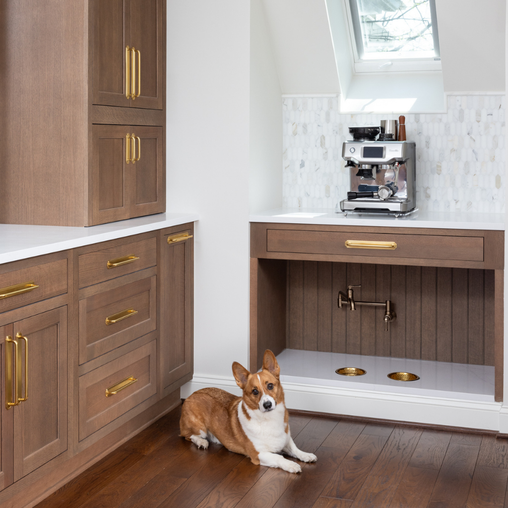 Dog sitting beside a custom built-in food and water station in a beautifully remodeled kitchen featuring white cabinetry, hardwood floors, and modern finishes.